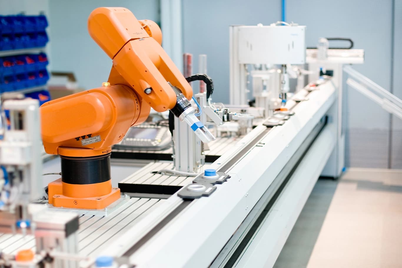 Orange articulated robotic arm operating along an automated industrial assembly line with pneumatic components