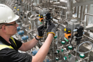 Industrial technician in hard hat and safety vest adjusting solenoid valves on a stainless steel pneumatic manifold system