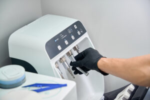 Gloved hand removing a piece from an automated instrument reprocessing and maintenance unit in a medical setting Gloved hand removing a piece from an automated instrument reprocessing and maintenance unit in a medical setting